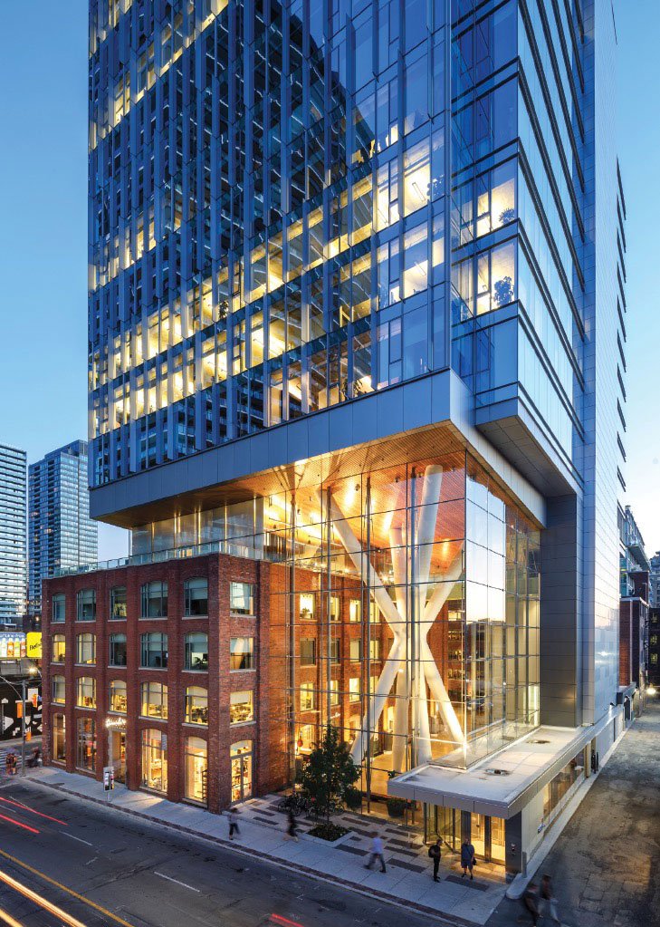 Illuminated glass tower over heritage brick podium at dusk